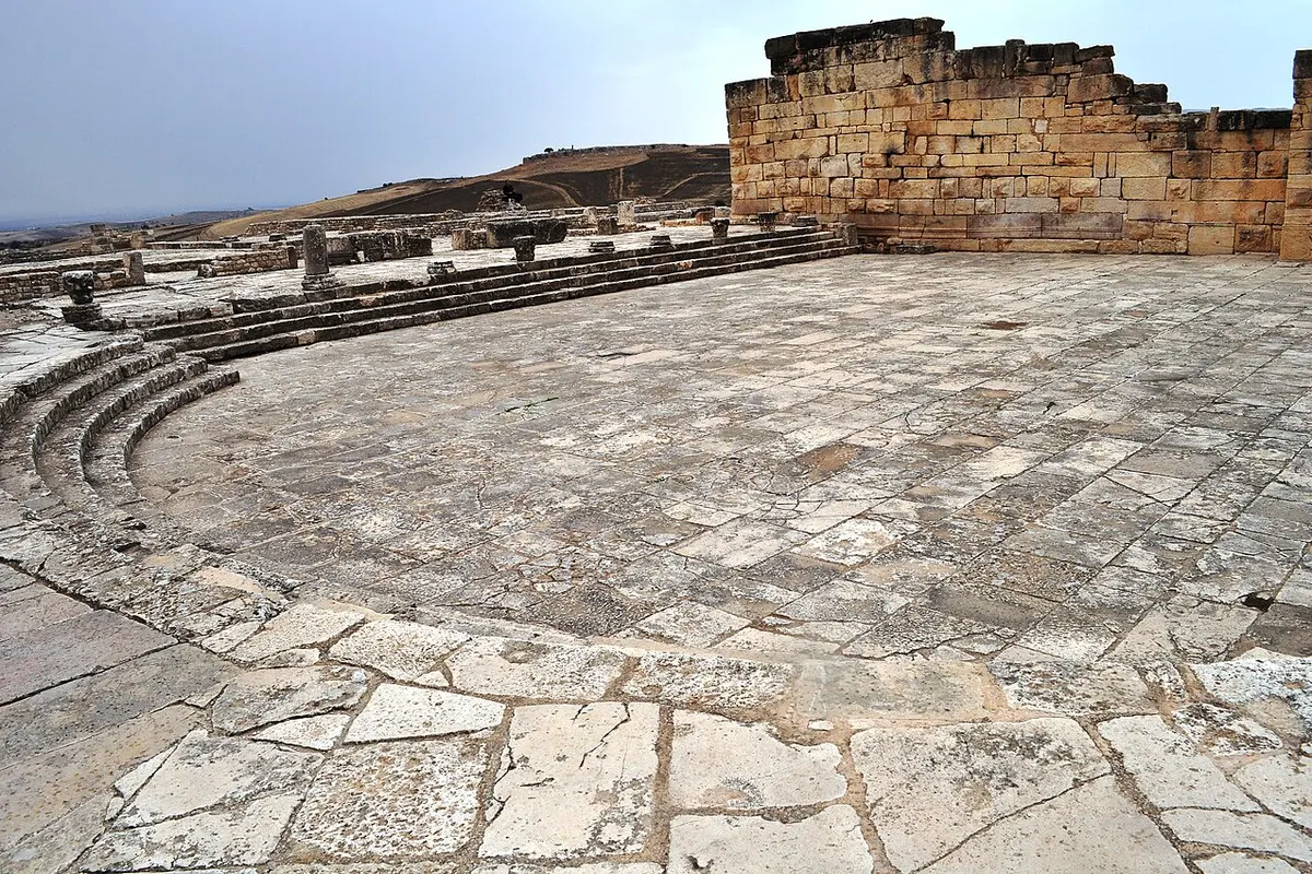A wide paved square at Dougga with a stepped edge on the left and a stone wall rising on the right